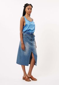 Satijnen blauwe tanktop gecombineerd met een hoog opgesneden denim maxi rok met een split aan de voorkant en bruine haksandalen.
