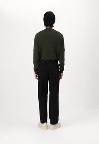 Grön stickad tröja, svarta byxor och ljusa sneakers. Tröjan har rund hals och figursydda ärmar med texturerad tyg.