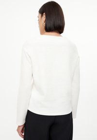 Witte textuur lange mouw top met een bladenpatroon, voorzien van een ronde halslijn en een ontspannen pasvorm, gecombineerd met zwarte broek.