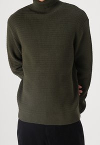 Pull-over vert foncé avec un motif en tricot gaufré, col montant et poignets côtelés. Coupe ample.