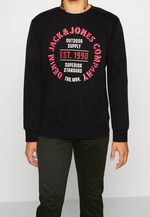 Sweat-shirt noir à manches longues avec texte circulaire rouge et blanc « Jack & Jones Company Denim » et « Est. 1990 Superior Standard » sur le devant.