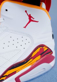 Biele kožené tenisky s červeným logom Jumpman, farebnými abstraktnými akcentami v žltej a červenej na podrážke a textúrovanými detailmi na vrchnej časti.