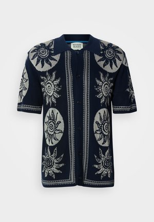 Cardigan à manches courtes bleu marine avec un motif soleil en gris clair, boutonnage devant, et col contrastant avec un tricotage détaillé et élaboré.