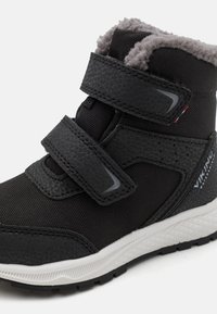 Schwarzer wasserdichter Stiefel mit strukturiertem Design, zwei Klettverschlüssen, weicher grauer Innenauskleidung und einer weißen Gummisohle mit Profil.