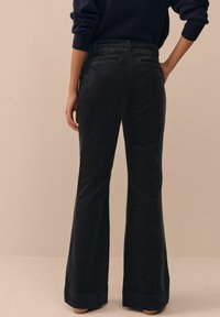 Black corduroy flared pants with a smooth texture, two back pockets, and a hemmed bottom. Features a standard waistband design.