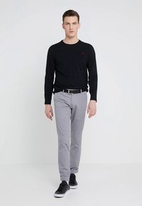 Svart langermet skjorte, grå bukser, svart belte og svarte joggesko. Skjorten har en liten rød logo på brystet.