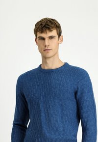 Niebieski dziergany sweter z teksturowanym wzorem, okrągłym dekoltem i długimi rękawami, wykonany z miękkiej mieszanki wełny.