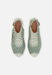 Chaussures ouvertes à l'avant en tissu vert avec une bride arrière, arborant une semelle intérieure à motif avec des designs de feuilles clairs et foncés.