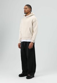 Beige hoodie met een kangoeroezak en een ontspannen pasvorm; gecombineerd met zwarte wijde jeans en chunky zwarte schoenen met contrasterende veters.