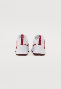 Baskets de sport blanches avec des accents rouges, design arrondi, semelle en caoutchouc texturée et languettes de tirage sur les talons avec un détail de logo.