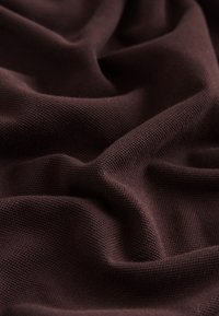 Tissu tricoté brun foncé avec une texture visible et des plis doux créant des ombres et des reflets sur toute la surface.