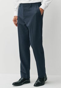 Marineblau gestreifte Hosen aus einem glatten Stoff, mit flachem Bund, Seitentaschen und taillierter Passform, kombiniert mit schwarzen Schuhen.