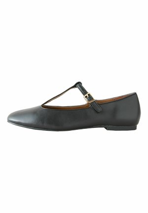 Black leather flat shoe with a T-strap and gold buckle, pointed toe, and low heel.