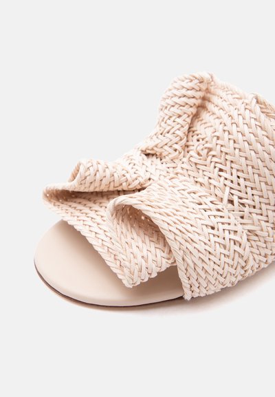 Κοντινό πλάνο από μπεζ υφαντή σαγιονάρα με φαρδιά υφή λουρί και ανοιχτό δάχτυλο σε ανοιχτό φόντο.