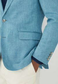 Blazer in lino azzurro chiaro con revers a punta, chiusura con un bottone singolo e polsini con tre bottoni. Include una tasca sul petto e tasche laterali.