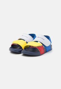 Tofarvede sandaler med en marineblå sål, der har blå, gule og røde remme. Glat syntetisk materiale med Velcro-lukninger og en tekstureret indersål.