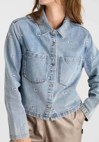 Lichtblauwe spijkerjack met geborduurde logo's, twee voorzakken, knoopsluitingen en een klassieke kraag. Textuurstof met een ontspannen pasvorm.