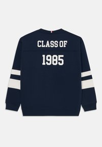 Marinblå sweatshirt med vit text "CLASS OF 1985" på baksidan. Har vita och marinblå ränder på ärmarna. Mjuk, blandad bomullsstruktur.