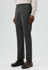 Grijze op maat gemaakte broek met een gladde textuur, voorzien van een vierkante tailleband, zijknop en subtiele omgeslagen zomen, gecombineerd met donkere loafers.