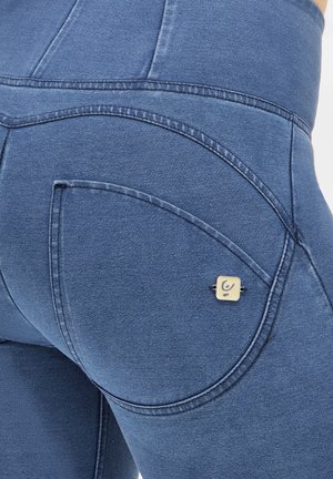 Blaue Denim-Leggings mit einem geschwungenen Taschendesign, minimaler Naht und einem quadratischen Hardware-Element in der Nähe der rechten Tasche.