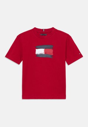 Red cotton t-shirt featuring a graphic design with brushstroke accents in blue, white, and red. Crew neckline and short sleeves.
