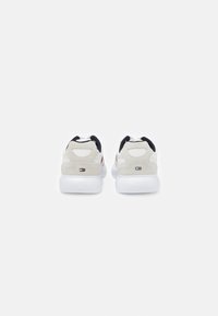 Sneakers bianchi con tallone in suede grigio e dettagli neri. Presentano un design elegante e un logo sul retro, con una suola bianca ammortizzata.