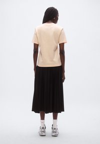 Lyse ferskenfarvet kortærmet t-shirt kombineret med en sort plisseret nederdel, båret med hvide og sorte sneakers og hvide ankelsokker.