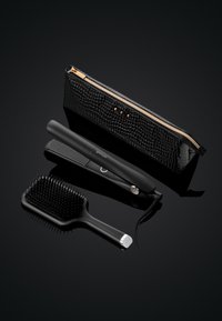 Zwart gelakte leren etui met gouden rits, naast een zwarte haarstyler en een zwarte paddleborstel met plastic haren en een gestructureerd handvat.