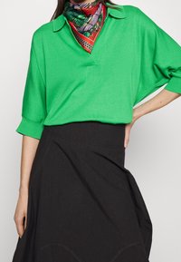 Polo a maniche corte verde in maglina con colletto, caratterizzato da una sottile trama. Abbinato a una gonna nera, che enfatizza i colori a contrasto.