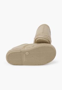 Béžová látková obuv na slip-on s textúrovanou gumovou podrážkou. Obsahuje opletené akcenty pozdĺž hornej hrany a malé logo na boku.