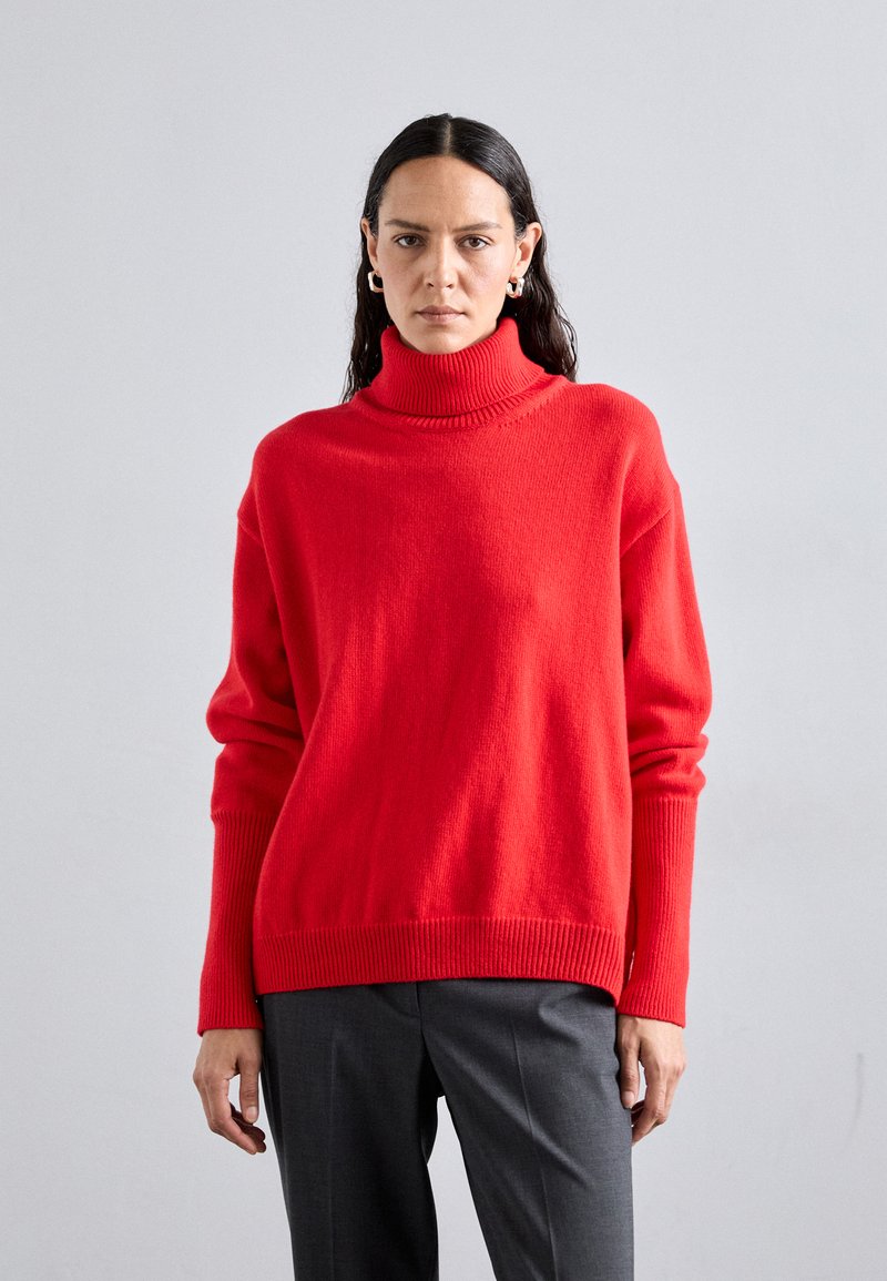 Red knit turtleneck sweater with a relaxed fit, ribbed cuffs, and hem; paired with gray tailored trousers. Smooth texture, medium thickness.