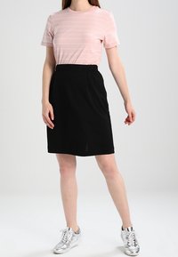 Světle růžové pruhované tričko v kombinaci s černou áčkovou sukní, doplněné stříbrnými teniskami. Oblečení má ležérní design a jemné textury.
