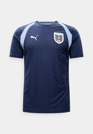 Maglia sportiva blu scuro con pannelli color azzurro chiaro sulle spalle, motivo astratto sottile, logo Puma sul petto a destra e stemma del calcio austriaco sul petto a sinistra.