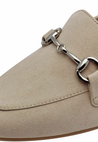 Bežid slip-on kingad, mis on valmistatud pehmest kangast ja millel on sile tekstuur. Üleval on hõbetoonne metallketi aksessuaar.