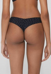 Granatowa stringi w kropki o gładkiej fakturze i minimalnym pokryciu, z miękkim pasem w talii oraz delikatnie zaokrąglonym tyłem.