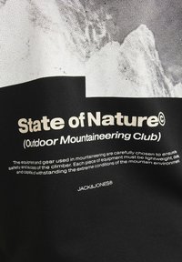 Melna auduma ar baltu tekstu, kurā ir rakstīts "Daba stāvoklis" un informācija par kalnu kāpšanas aprīkojumu. Iekļauj logo "JACK&JONES®."