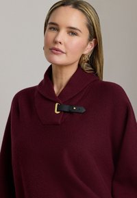 Vinrød sweater med en rullekrave, der har en sort læderrem og detalje med guldbuckle. Tekstureret stof med en afslappet pasform.