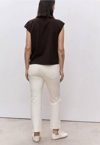 Top marrone a maniche corte con scollatura rotonda, abbinato a jeans bianchi a gamba dritta con orli sfrangiati e scarpe da ginnastica bianche.