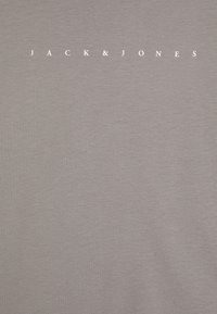 Pelēks kokvilnas T-krekls ar apaļu apkakli un tekstu "JACK & JONES" baltā krāsā, centrēts uz krūtīm. Mīksta tekstūra.