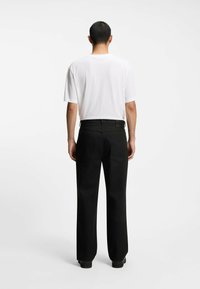 Pantaloni neri a gamba larga con una texture liscia, dotati di una cintura con etichetta. Abbinati a una maglietta bianca semplice a maniche corte.