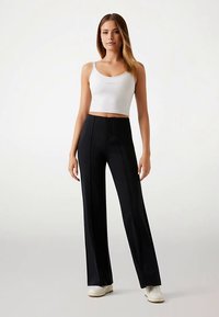 Pantaloni negri cu picioare largi, cu un design croit, având pliuri frontale și o textură netedă, asortați cu un top alb scurt.