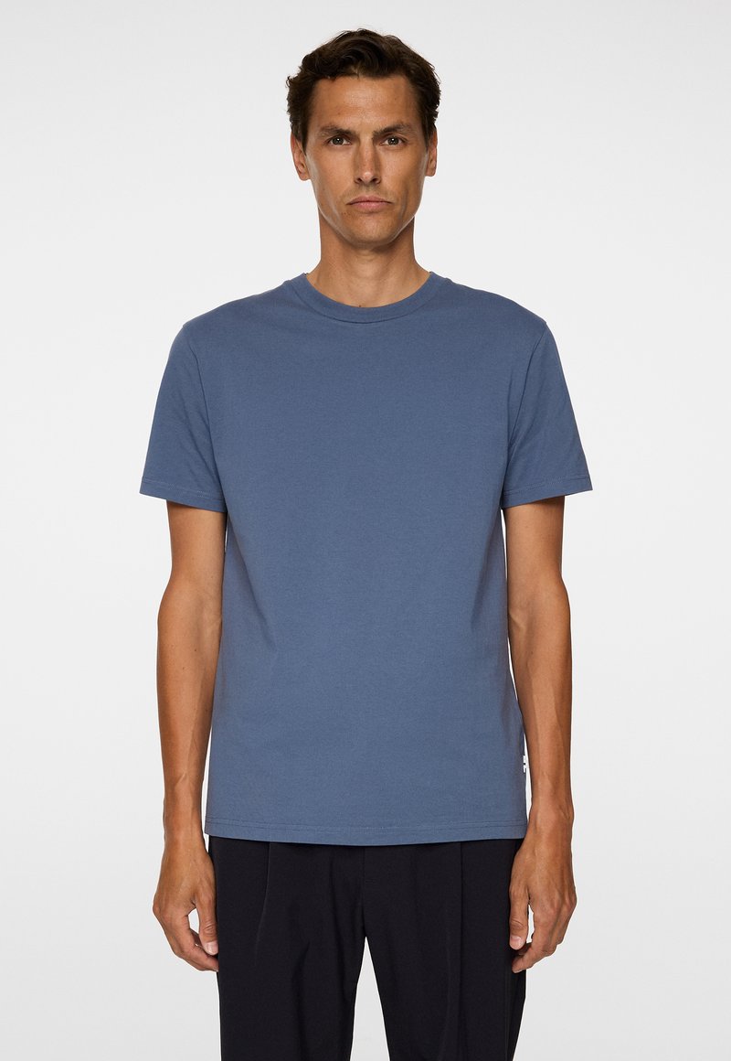 T-shirt à manches courtes en coton bleu atténué, avec un ourlet droit et un détail logo subtil en bas à gauche.