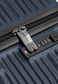 Gros plan sur une valise bleue texturée avec des tirettes de zip doubles portant l'inscription "REDOLZ", sécurisée par un verrou à combinaison approuvé par la TSA.