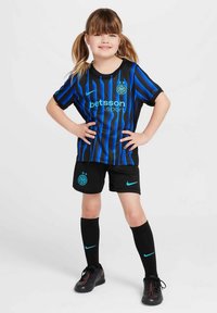 Črna nogometna majica z modrimi navpičnimi črtami, z okroglim logotipom in napisom. Črne kratke hlače, črne nogavice do kolen in črni nogometni čevlji.