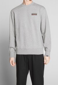 Sudadera gris con cuello redondo, puños y dobladillo acanalados. Presenta un pequeño logotipo rectangular en negro y naranja en el pecho.