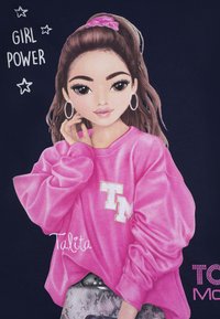 Illustrazione di una ragazza con lunghi capelli castani che indossa una felpa rosa oversize con la scritta "TM". Lo sfondo è blu scuro con la scritta "GIRL POWER" e stelle.