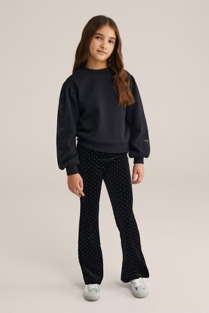 Sudadera negra con mangas abullonadas y detalles de estrellas en los brazos, combinada con pantalones de terciopelo negro acampanados con lunares blancos. Zapatillas blancas.