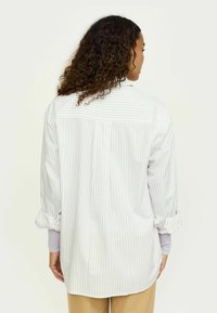 Cămașă cu dungi cu mâneci lungi în culori deschise, având o croială relaxată, închidere cu nasturi pe spate și mâneci suflecate cu manșete contrastante.