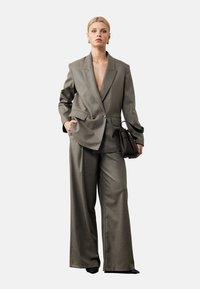 Grijze op maat gemaakte pak met een dubbelzijdige blazer en wijde pantalon. De stof heeft een gladde textuur, met een diepe V-hals en zijzakken.
