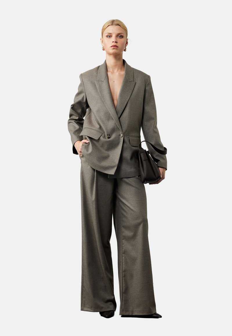 Grijze op maat gemaakte pak met een dubbelzijdige blazer en wijde pantalon. De stof heeft een gladde textuur, met een diepe V-hals en zijzakken.